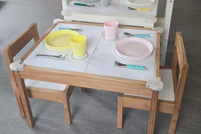 Petite table et chaises à hauteur d'enfant, avec des sets où l'assiette, le verre et les couverts sont dessinés
